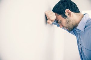 Depressed man with fist clenched leaning his head against a wall