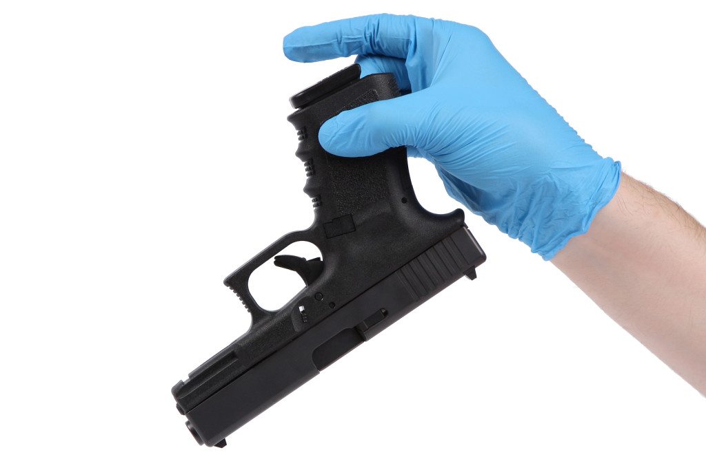 man wearing blue latex glove holds up gun as evidence